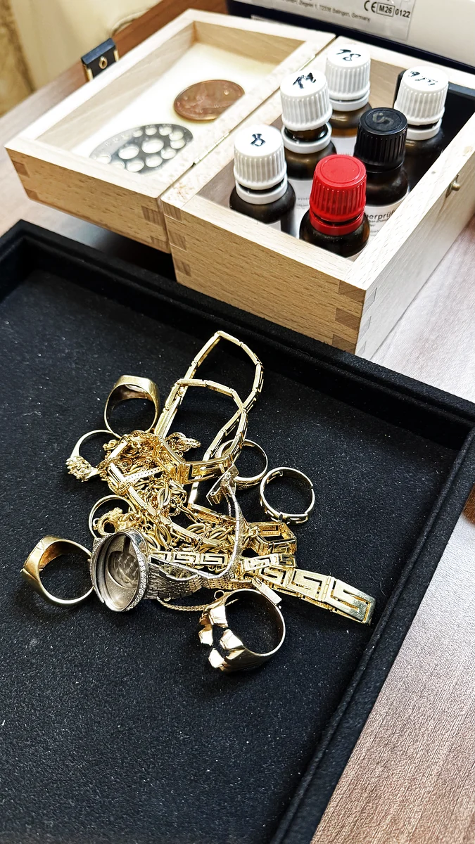 Bruchgold und Schmuckreste neben der genormten Prüfsäuren-Holzbox und dem natürlichen Prüfstein