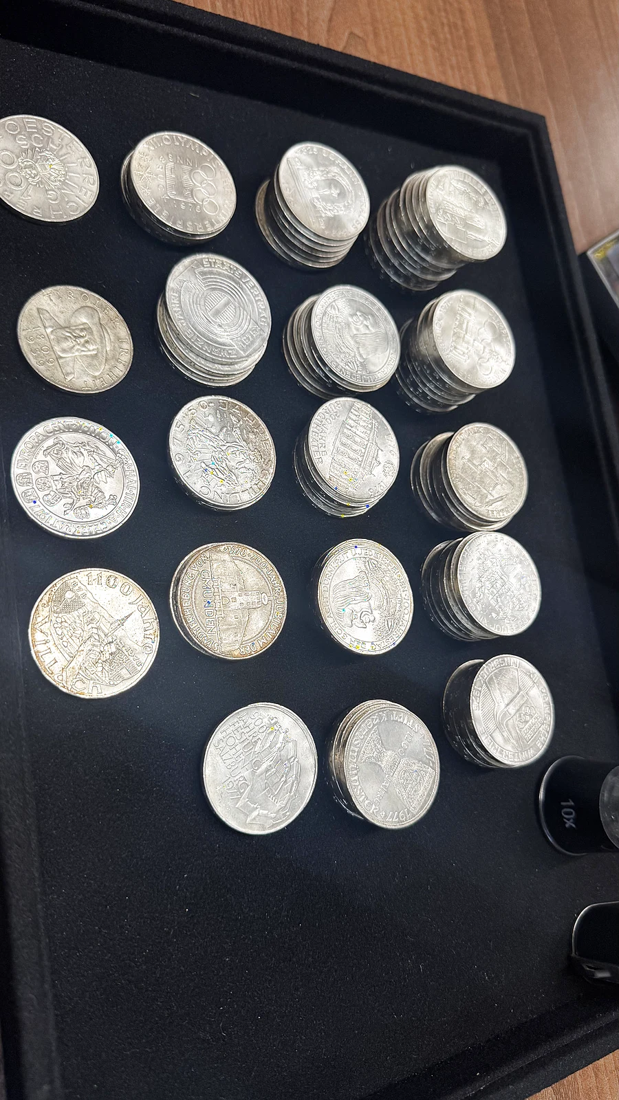 Österreichische Silberschillinge auf schwarzem Samtteller neben einer 10x Juwelierlupe bei Gold & More